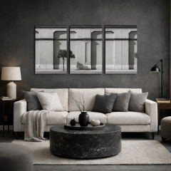 Three panel black and white classical facade wall art displayed above neutral sofa in modern dark living room interior